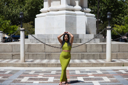 Beautiful young Spanish brunette woman in green dress doing different body postures in the town hall square in Seville, Spain. Behind are typical orange trees in Mediterranean style citiesの写真素材