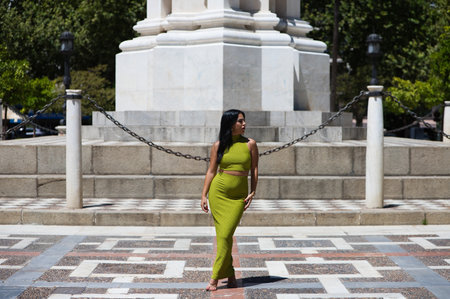 Beautiful young Spanish brunette woman in green dress doing different body postures in the town hall square in Seville, Spain. Behind are typical orange trees in Mediterranean style citiesの写真素材