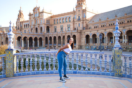 young, beautiful, brunette moroccan woman dressed in white top and jeans in Seville's Spain square. Woman enjoys her vacation walking around the city in Andalusia, Spain. Travel and tourism conceptの写真素材