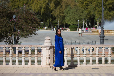 young and beautiful moroccan woman in blue abaya, typical arabian costume, walking along the canal in the square of spain in Seville, a world heritage site, on a sunny day. travel conceptの写真素材