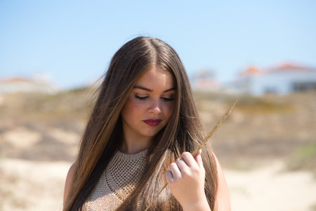 Portrait of a beautiful young blonde woman with long hair holding a wild ear of corn in her hand and bringing it close to her face. The woman is wearing makeup and is dressed casuallyの写真素材