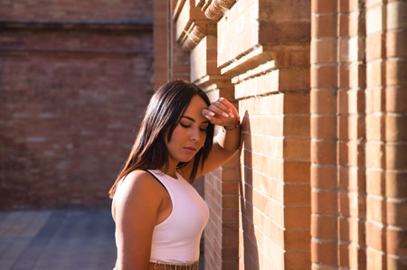 pretty young brunette woman rests her head on her arm on the wall and looks down.の写真素材