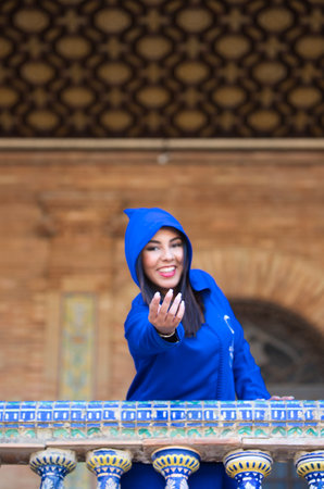 Moroccan woman, brunette, young and beautiful dressed with abaya, leaning out of the balcony and extends her hand.の写真素材