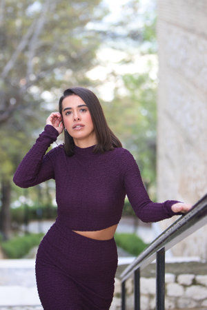 pretty young woman dressed in elegant purple dress climbs the stairs holding on to the metal railing with her hand. The woman makes different expressions and gesturesの写真素材