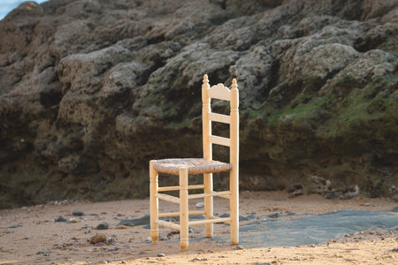 An old wooden chair on the shore of the beach next to the rocksの写真素材
