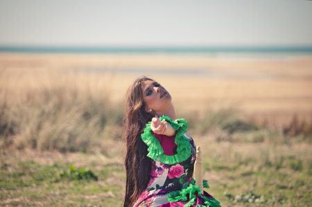 A dancer in a floral patterned dress with green ruffles, seated outdoors with the ocean visible on the horizonの写真素材