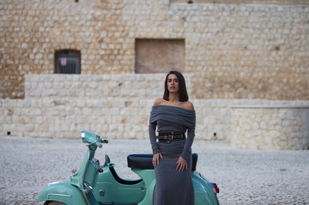 Young woman dressed in gray and black boots sitting on the seat of a turquoise sidecar. The woman makes different expressionsの写真素材