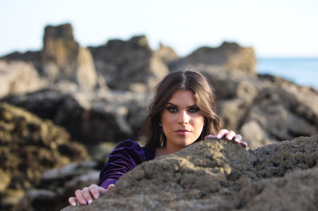 beautiful young woman dancing flamenco among the rocks by the seashore, wearing a purple velvet dress with ruffles. The gypsy woman makes different expressions with her face and handsの写真素材