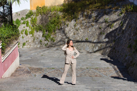Young woman walks up the stairs of a street. The woman is wearing a beige suit jacket. The woman is happy and makes different body postures. Photo taken from aboveの写真素材