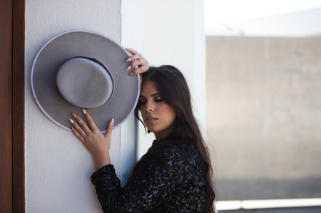 portrait of a Latin woman, young and beautiful flamenco dancer with her hands and arms on the wall holding a hat. The woman looks at the camera with a serious and sensual faceの写真素材