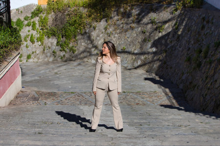 Young and beautiful blonde woman walks up the stairs of a street. The woman is wearing a beige suit jacket. The woman is happy and makes different body postures. Photo taken from aboveの写真素材