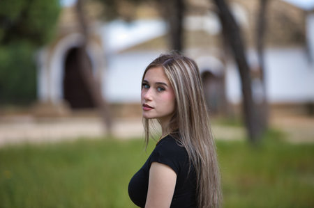 portrait of young and beautiful blonde woman, wearing jeans, black shirt walking in the countryside on a spring day. The woman has her back turned and is looking back for the photoの写真素材