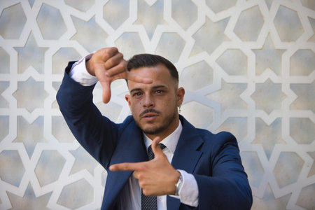 A young, handsome man wearing a suit and tie, making a frame gesture with his hands and fingers, looking at the camera while standing on an isolated white backgroundの写真素材