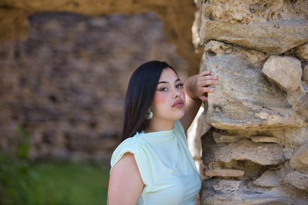 A beautiful Spanish teenager with long dark hair rests her hand on a stone wall.の写真素材