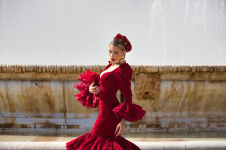 A beautiful woman dancing flamenco in a square in Seville, Spain. She is wearing a red dress with ruffles and dancing flamenco with great artistry. Flamenco, cultural heritage of humanityの写真素材