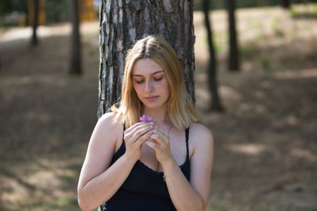 A young, beautiful, natural blonde woman holds a purple flower in her hands as she looks at it and smells it. Concept beauty and healthの写真素材