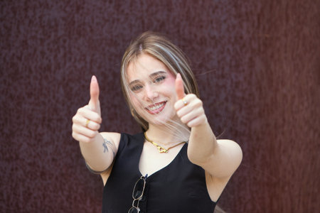 blonde woman with light eyes, young and beautiful, holds up the thumb of her two hands and makes a gesture that everything is fine, and it is correct. The woman is happy and smilesの写真素材