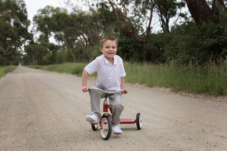 boy riding a trike on a dirt road
