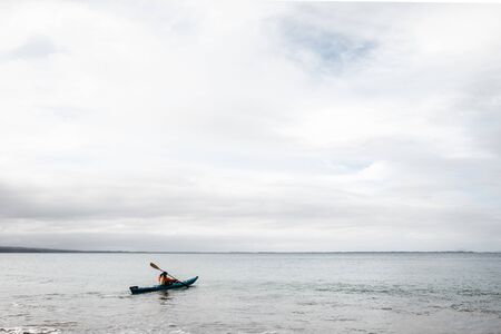A man using a blue Kayak in the Ocean on a still but cloudy dayの写真素材