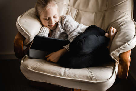 A young girl of caucasion descent sitting by a window watching programs on her tabletの写真素材