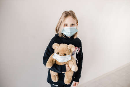 Young caucasion girl wearing a mask and holding a teddy bear who is also wearing a surgical mask during the COVID-19 corona virus pandemicの写真素材