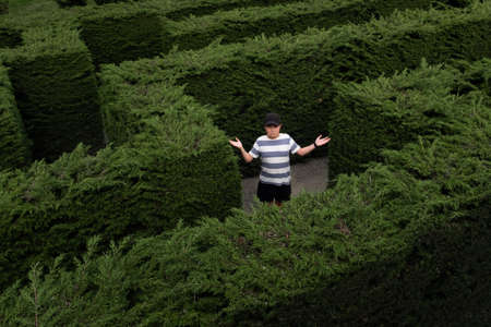 A boy in a hedge maze shrugging because he is lost