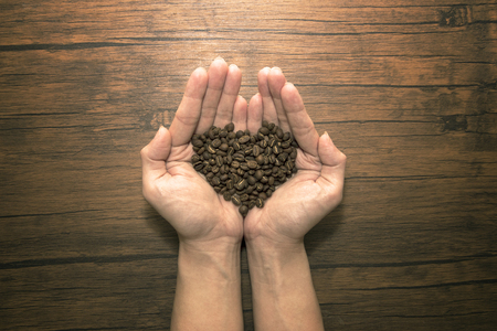 Heart-shaped coffee beans in the handsの写真素材
