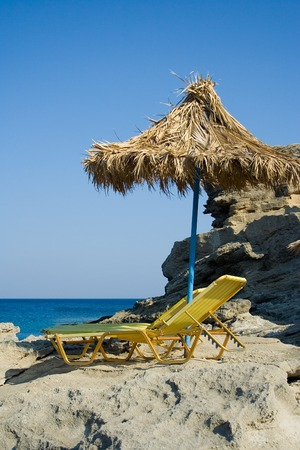Rocky beach, sun bed and palm umbrellaの写真素材