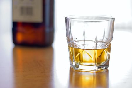 Glass of yellow whiskey and brown bottle on the tableの写真素材
