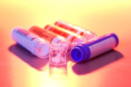 Close view of homeopathic medications in colored light - containers and small white balls in the cap