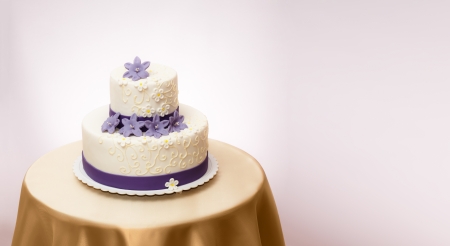 White wedding cake with violet marzipan flower decoration. Copy space on right