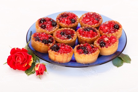 Berries cakes on blue plate, near with rose on white tableclothの写真素材