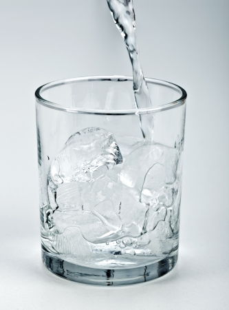 Water stream flowing into glass with ice cubesの写真素材