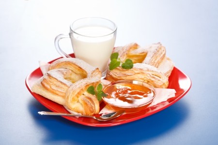 Light breakfast: two peach cakes, a cup of milk and jam on red plateの写真素材
