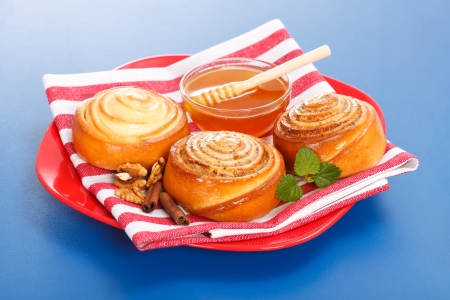 Cinnamon rolls and honey on red plate, blue backgroundの写真素材