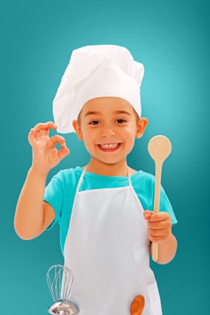 Cheerful little chef showing good taste and wooden spoonの写真素材