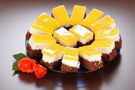 Three-layered yoghurt cakes with red roses on brown tableの写真素材