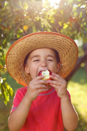 Boy in straw hat eating apple in orchardの写真素材