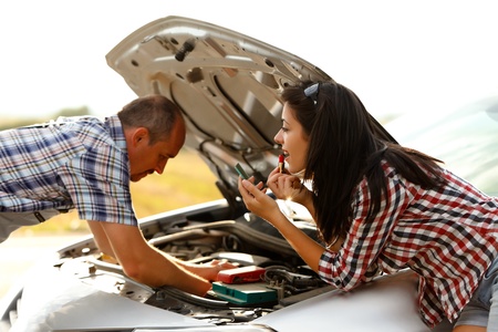 Woman applying lipstick while repairman works on fixing the broken car's engineの写真素材