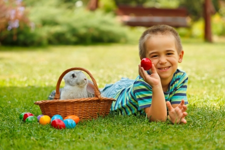 Smiling boy lying on green grass and showing an red easter eggの写真素材
