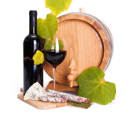 Red wine in bottle and glass with cheese and sausage snack in front of small barrelの写真素材