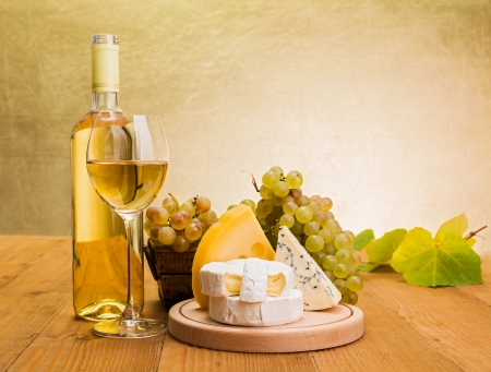White wine in bottle and glass with grapes, camembert, emmentaler and blue cheese snack, grape leaves decorationの写真素材
