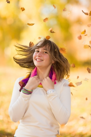 Joyful teen girl smiling and having fun in falling autumn leaves in a parkの写真素材