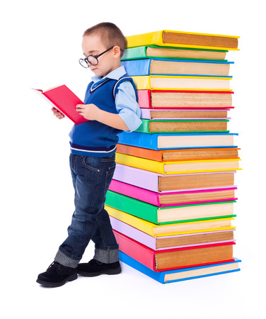 Little wise boy reading book near big stack of colorful booksの写真素材