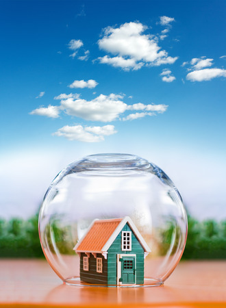 Insured house protected in glass sphere, under the cloudy bright sky