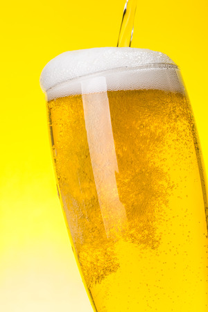 Macro of fresh beer being pured into glass on yellow backgroundの写真素材