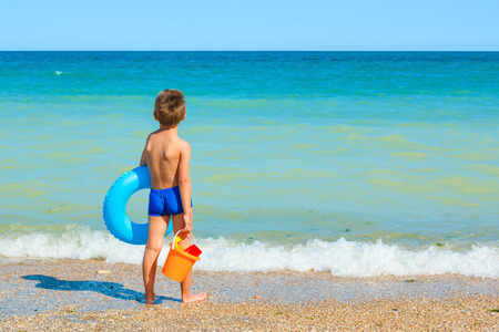 Child with toys and swimming ring, looking at the seaの写真素材