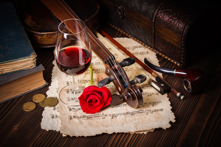 Romantic image detail with violin scroll, wine glass, books and red roseの写真素材
