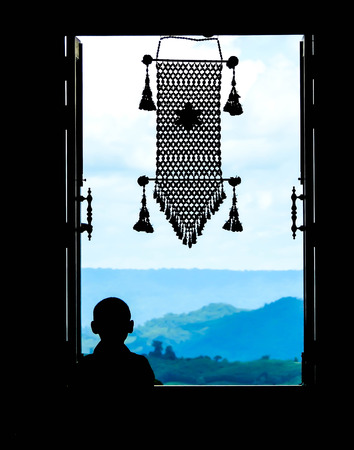 Neophyte at window in partial silhouette with thai  hanging mobile in a public temple, Wat Pa Phu Kon,Thailandの写真素材