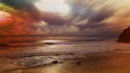 Stunning sunset and dramatic clouds across ocean waves on the shore.の写真素材